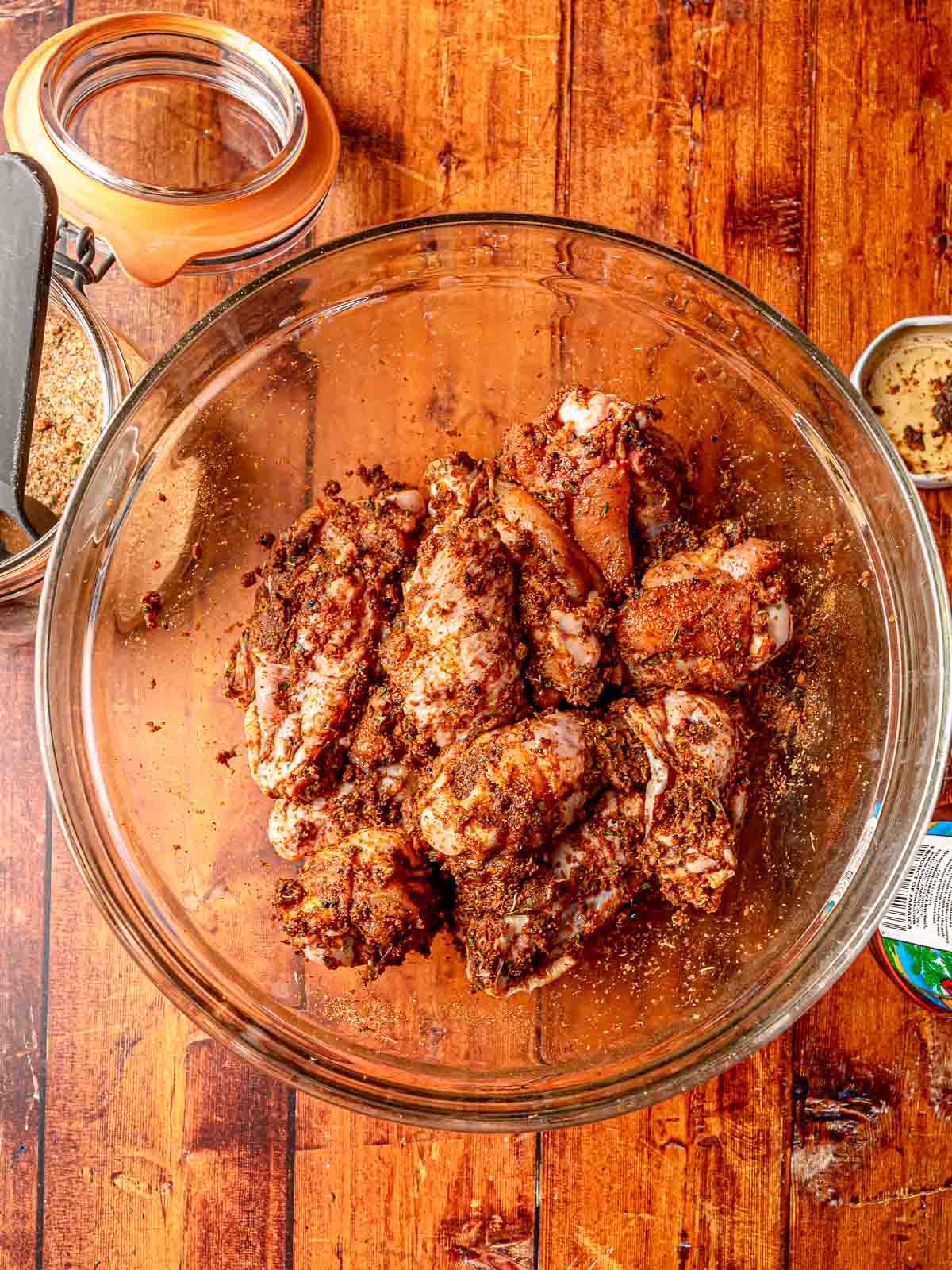 Chicken wings coated in jerk marinade and dry rub, resting in a glass mixing bowl.