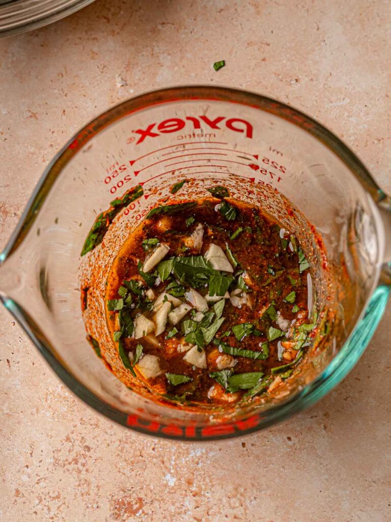 Marinade with chopped garlic and parsley in a glass measuring cup.
