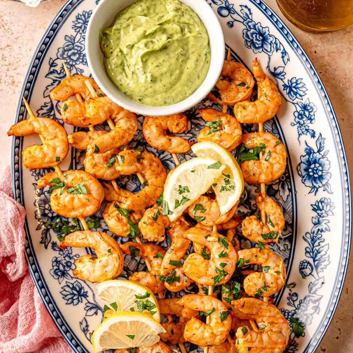 Smoked shrimp skewers arranged on a white platter with lemon wedges and fresh parsley.