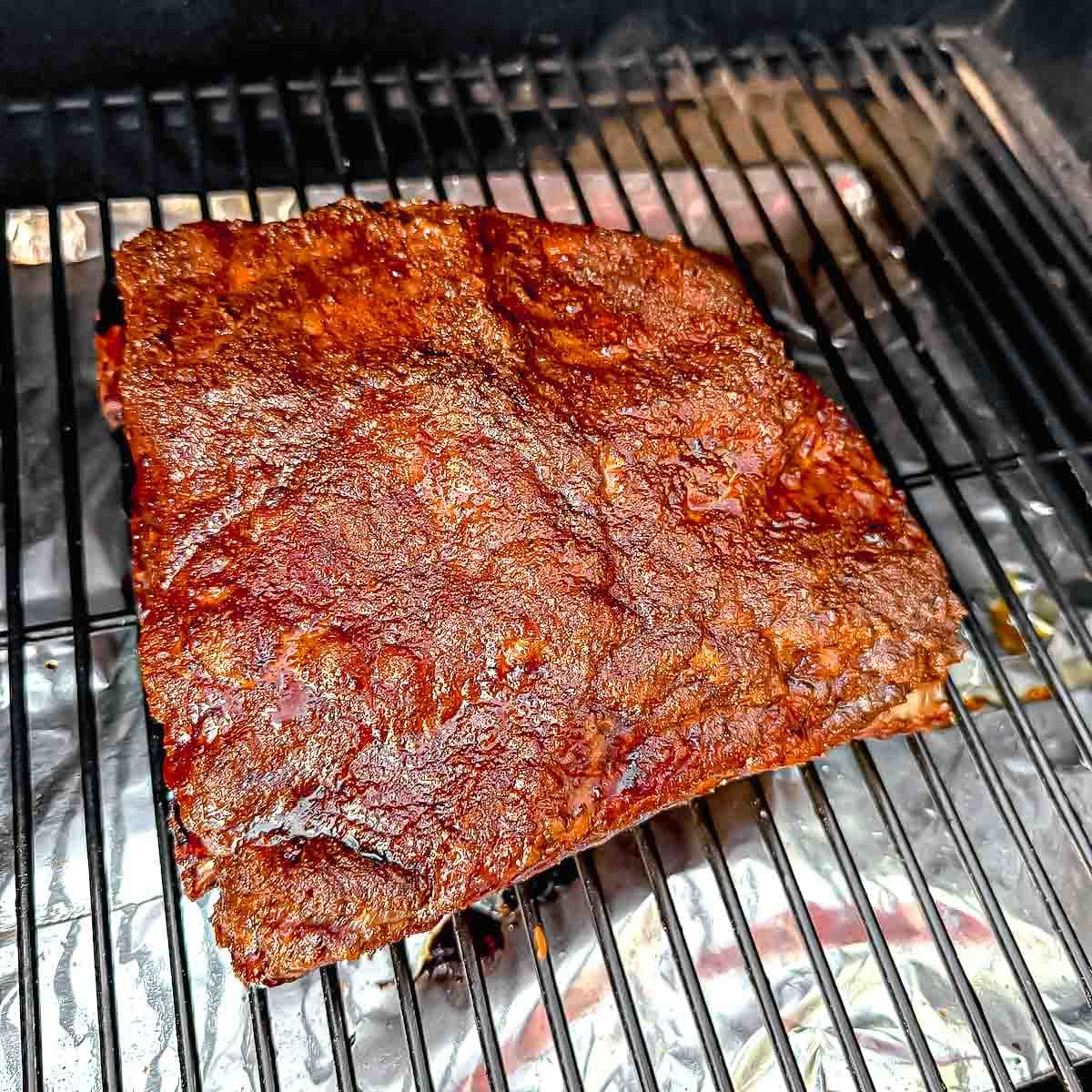 Smoked brisket resting on a pellet smoker grate with a deep, caramelized bark.