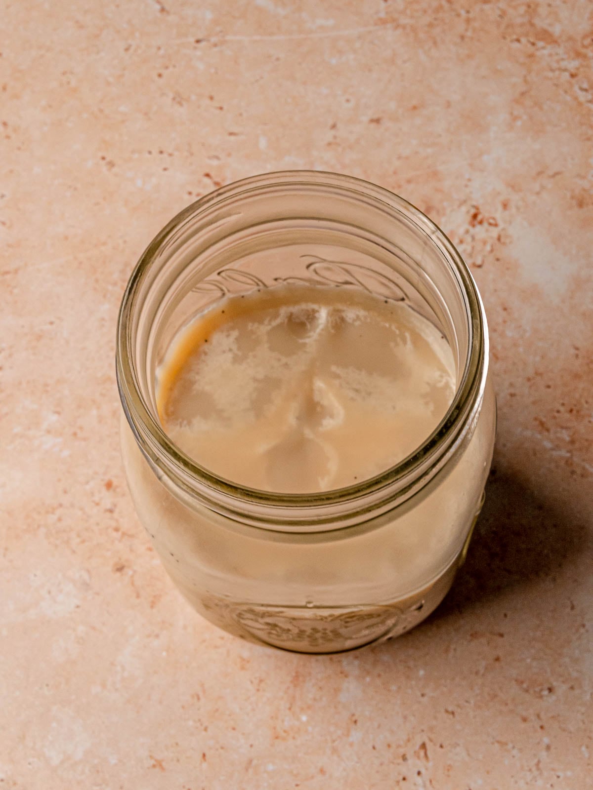 Freshly rendered beef tallow cooling and solidifying in a clear glass jar on the counter.