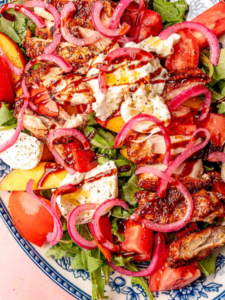 Fresh summer salad layered with smoked chicken, burrata, tomatoes, and peaches on a serving platter.