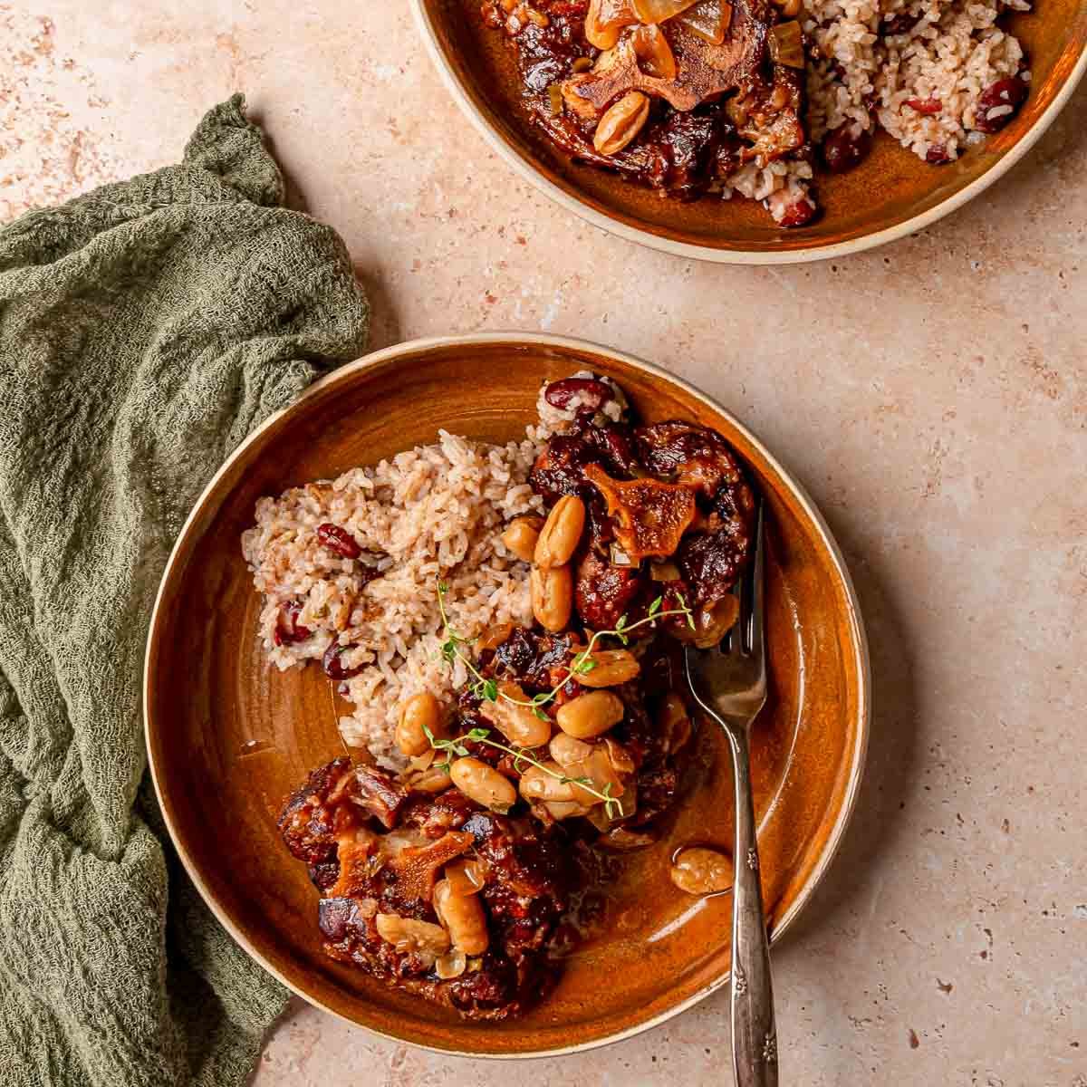 Plate of smoked oxtail with rice and peas, garnished with thyme sprigs.