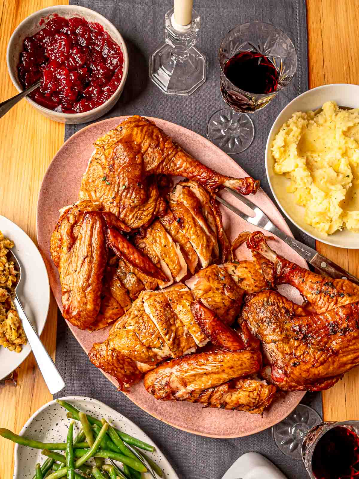 Smoked spatchcock turkey on a table with cranberry sauce, mashed potatoes, green beans and wine.