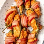 Smoked bacon-wrapped jalapeño poppers with creamy filling and crisp bacon on a white serving platter.