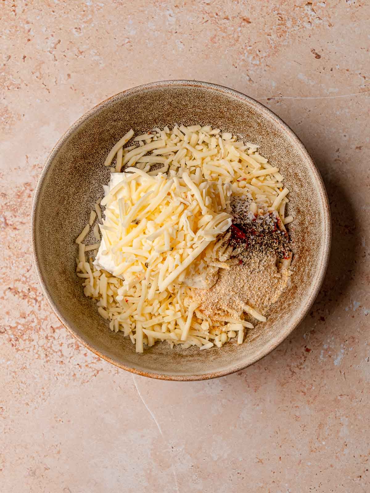 Cream cheese, shredded cheese, and spices combined in a bowl to make the filling for jalapeño poppers.
