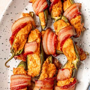 Smoked bacon-wrapped jalapeño poppers with creamy filling and crisp bacon on a white serving platter.