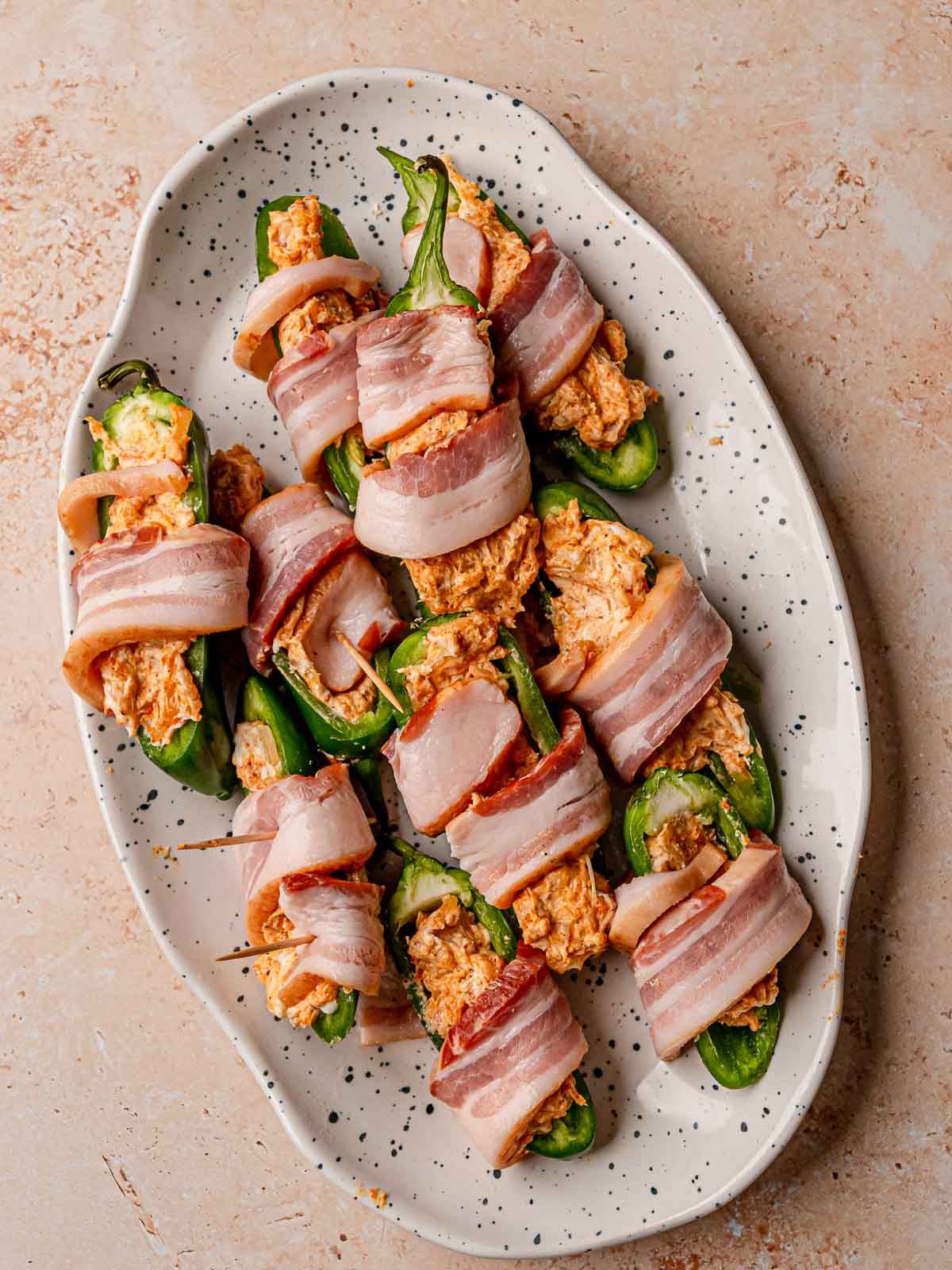 Cheese-stuffed jalapeños wrapped with bacon and secured with toothpicks before smoking.