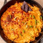Close-up of smoked buffalo chicken dip showing creamy chicken filling, melted cheese, and a tortilla chip dipped into the skillet.