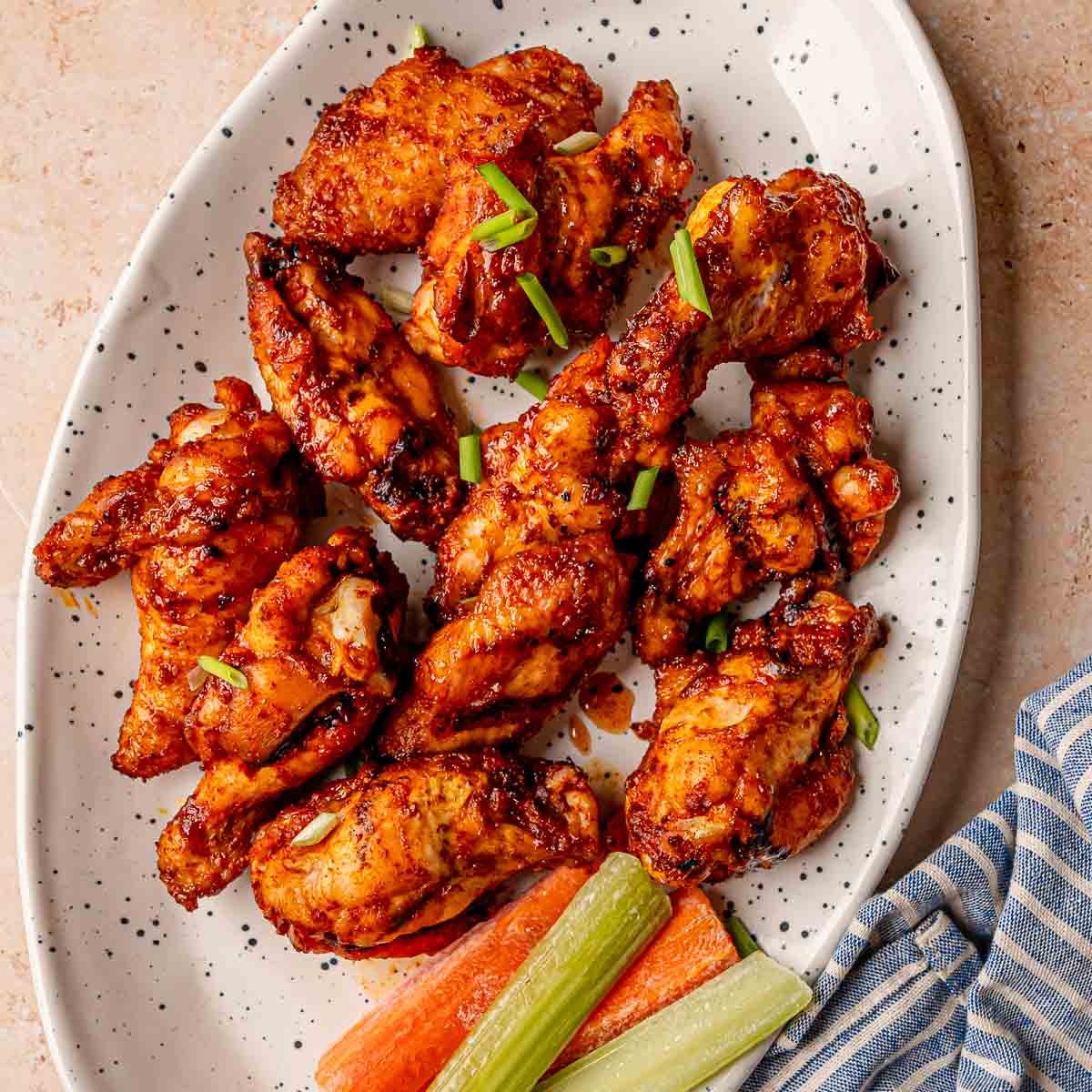 Smoked honey ginger chicken wings on a platter with celery, carrots, and green onion garnish.