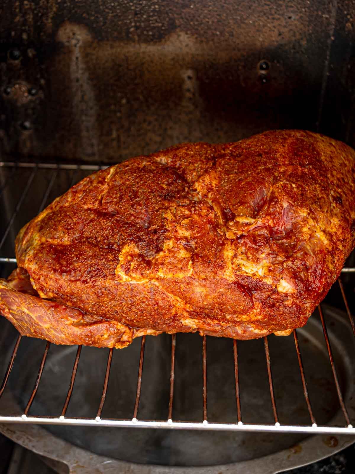 Seasoned pork shoulder on a rack inside an electric smoker.