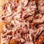Close view of shredded pulled pork on a cutting board with crispy bark pieces.
