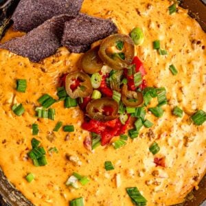 Smoked beef queso is topped with green onions, jalapeños, and diced tomatoes.