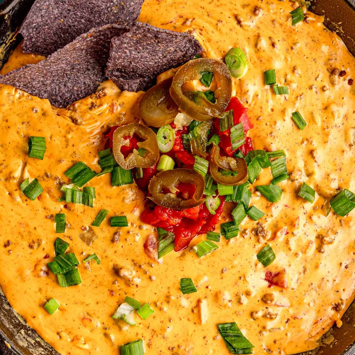 Smoked beef queso is topped with green onions, jalapeños, and diced tomatoes.