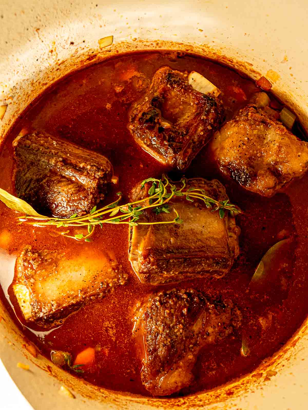 Smoked short ribs braising in a Dutch oven with red wine sauce and fresh herbs.