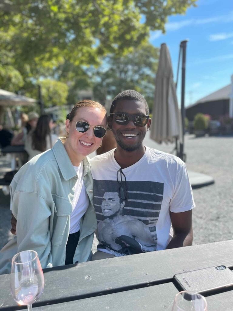 Sarah and Kadeem sitting at an outdoor table with glasses of rosé on a sunny day.