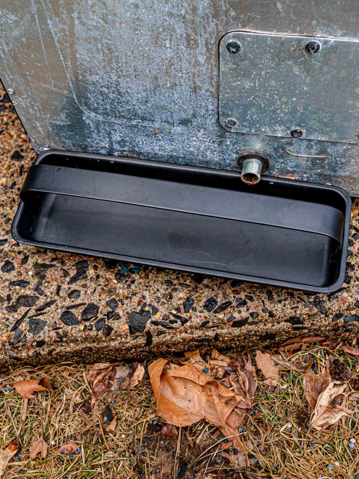 Drip tray positioned under the back of a Masterbuilt electric smoker.