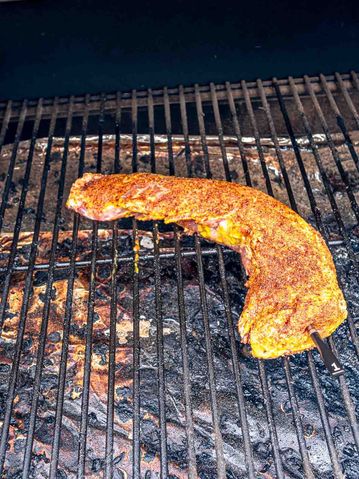 BBQ pork tenderloin smoking on the grates of an electric smoker with a thermometer probe inserted.
