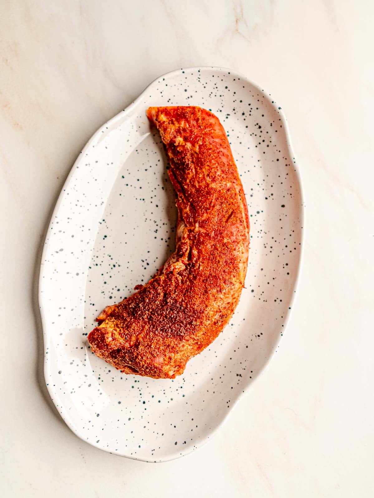 Smoked pork tenderloin resting on a white speckled platter after cooking.